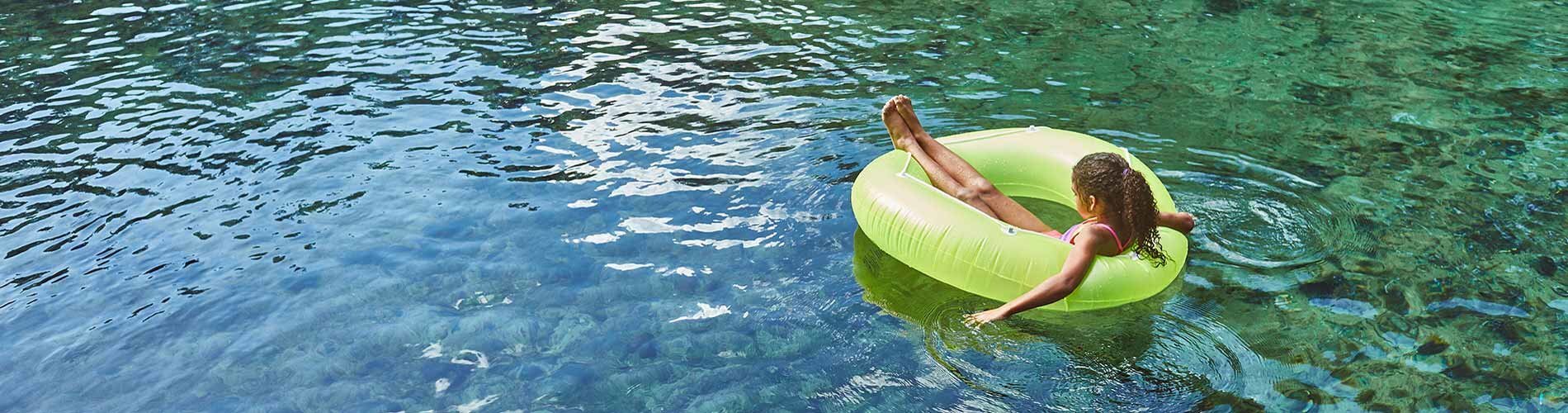 A young girl floating on a tube in a lake.